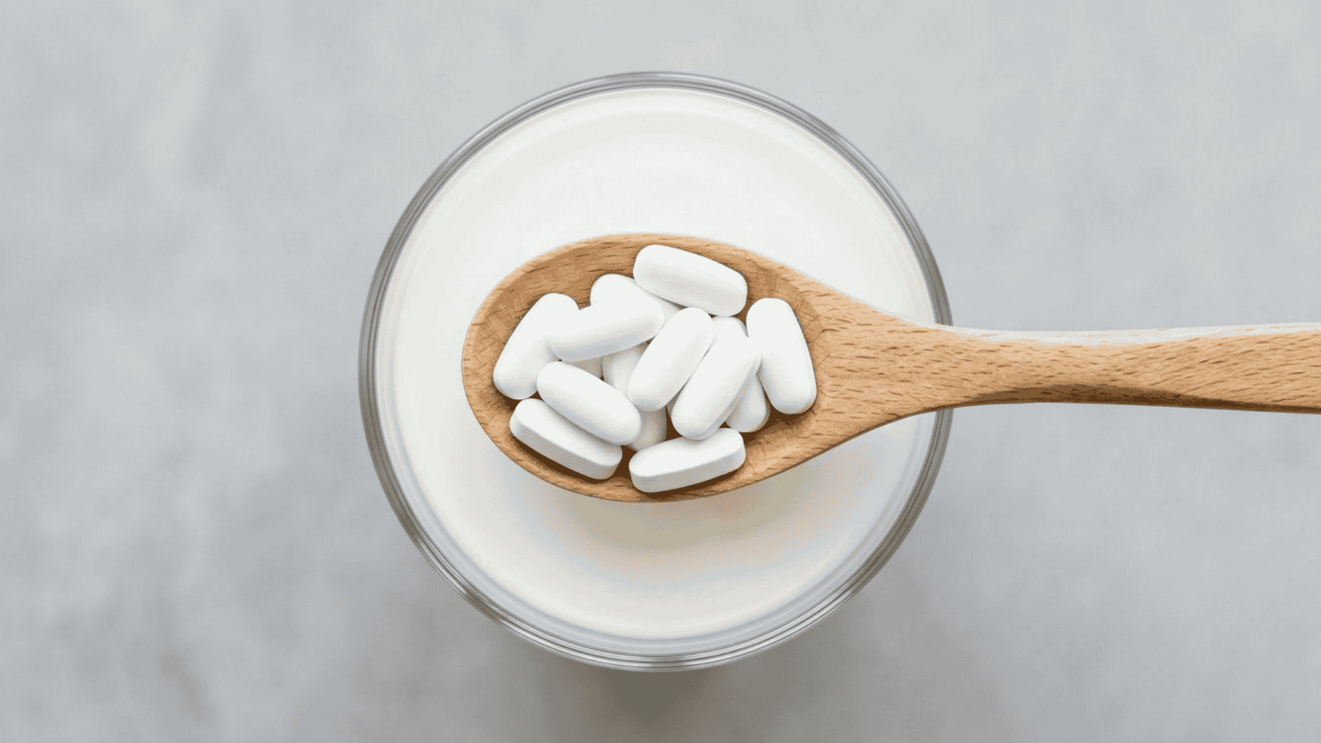 Wooden spoon with white tablets above a glass of milk, depicting calcium fortified food products and dietary supplementation.