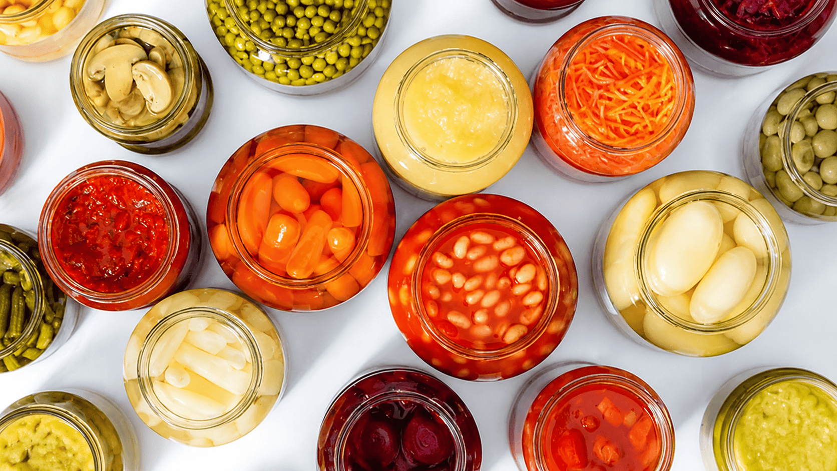 Assorted jars showing of pickled vegetables and preserved foods in brine, including carrots, beans, peas, and onions, where acetic acid provides antimicrobial preservation.
